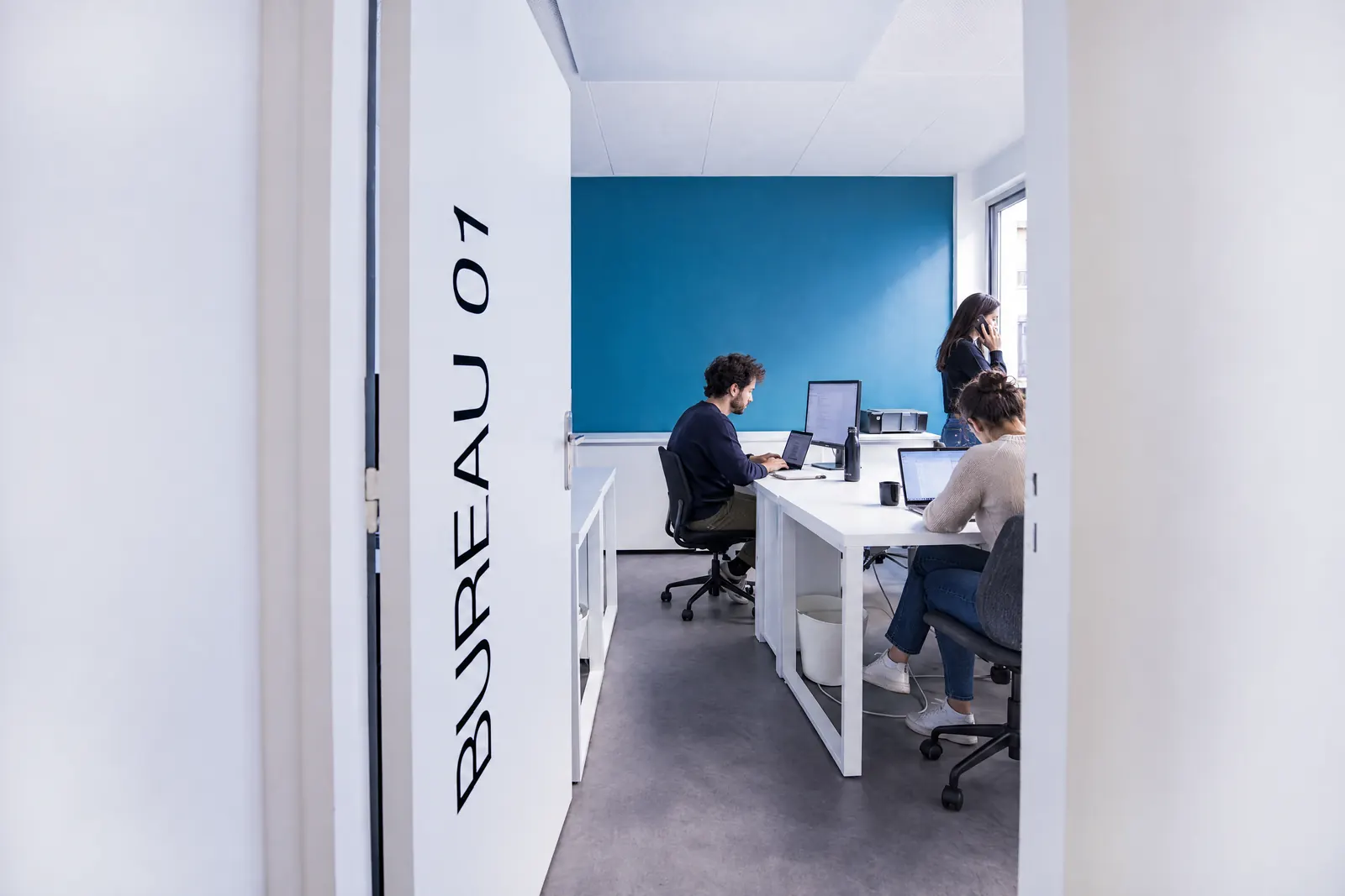 Une petite équipe au travail dans le bureau 01, au mur bleu pétrole.