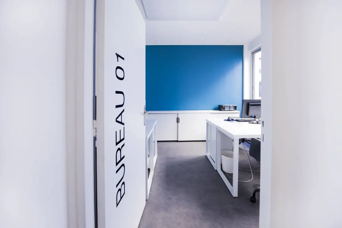 La porte ouverte du bureau 01, un bureau fermé meublé au mur bleu pétrole.