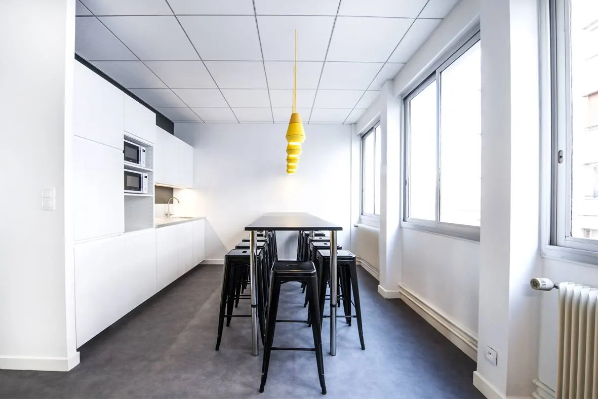 La cuisine blanche, sa longue table haute et sa suspension jaune.