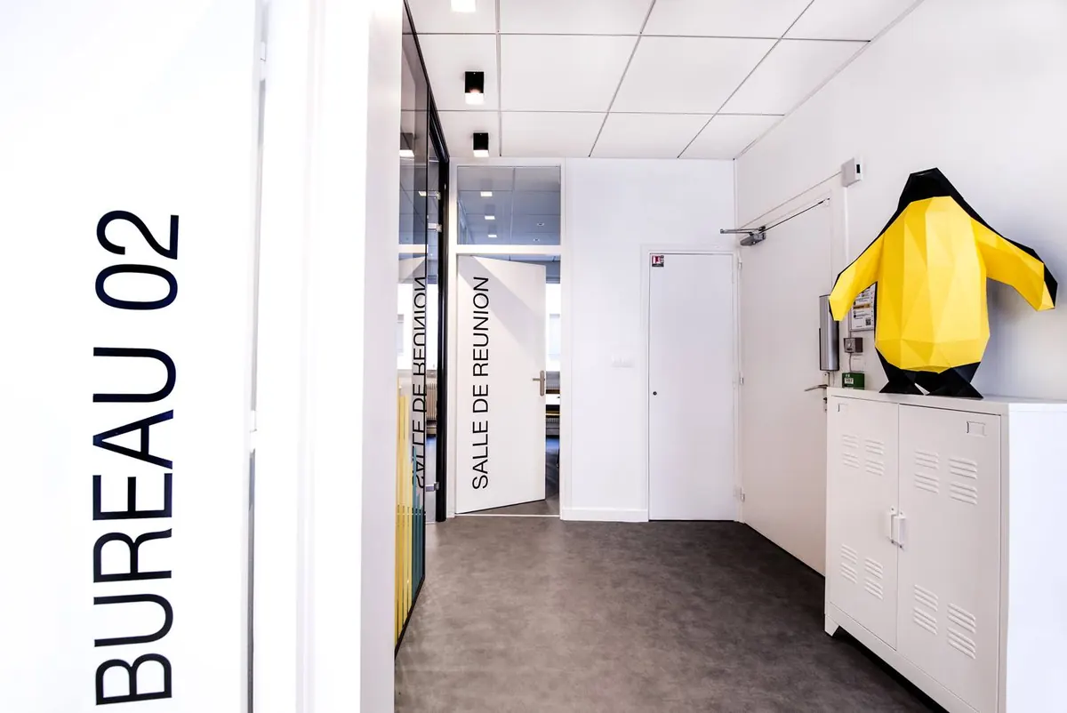 L'entrée, près du bureau 02 et de la salle de réunion, gardée par une grande statue de pingouin jaune.