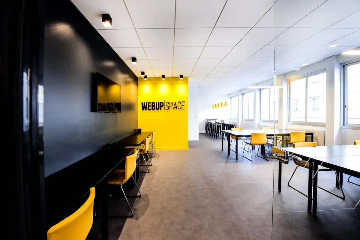 L'open space vide, mur noir, tables noires, chaises jaunes et mur jaune au logo.