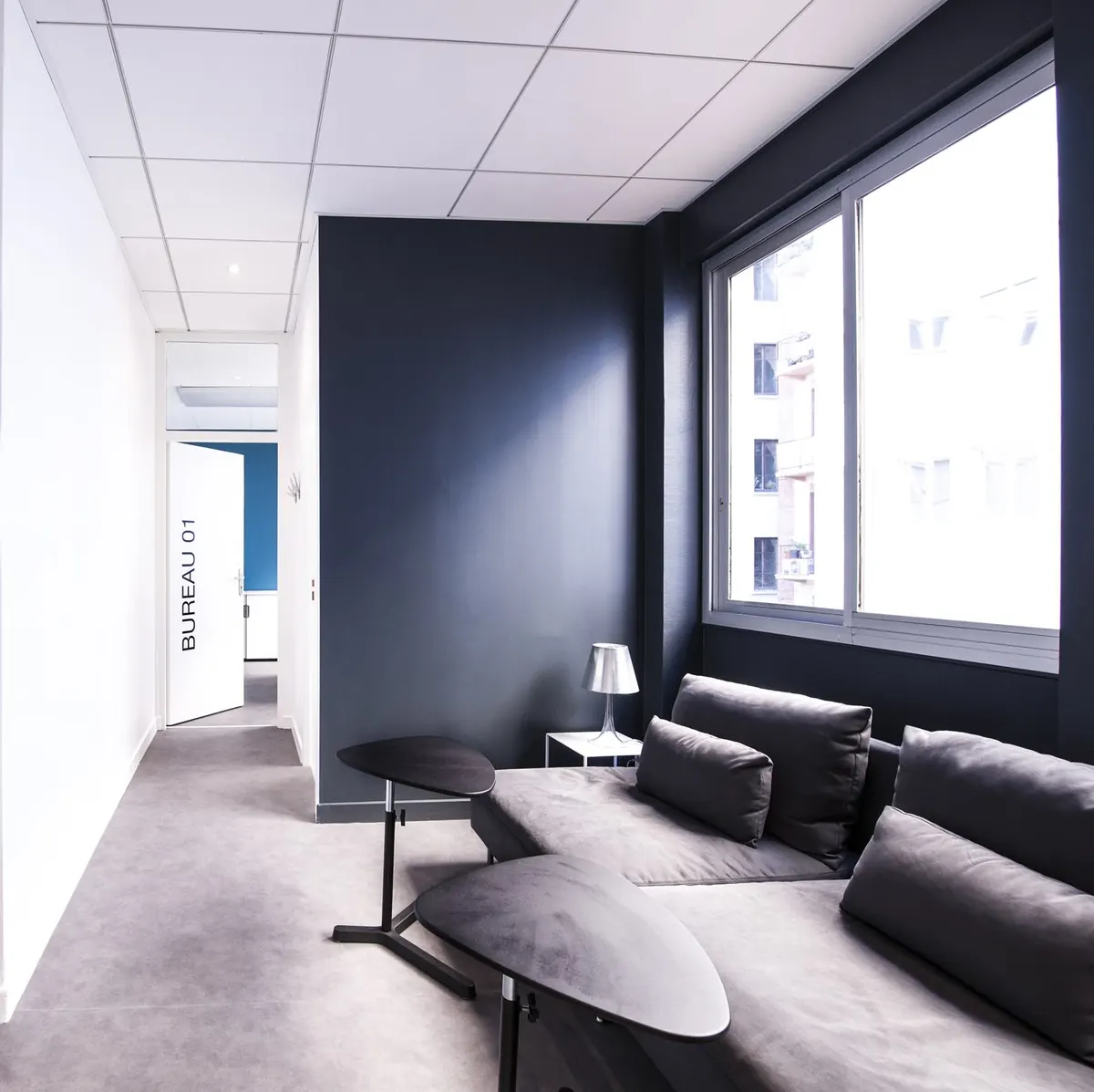 Le salon : canapé gris, table basse et grande fenêtre.